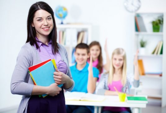 Happy teacher looking at camera with her students on background